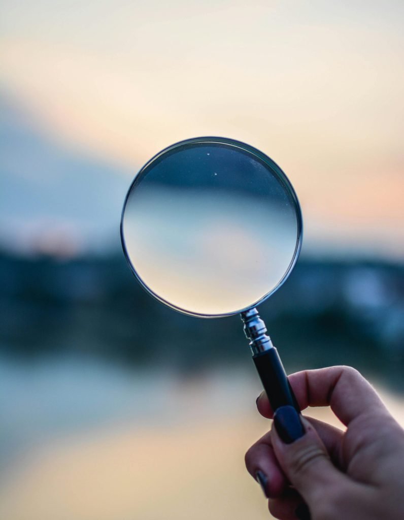 A magnifying glass held by a hand outdoors at sunset, focusing on exploration.