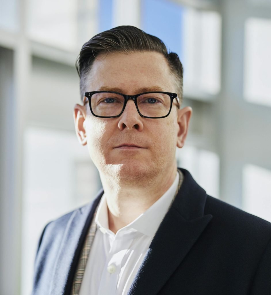Profile portrait of a confident business executive wearing eyeglasses in a sunlit office setting.